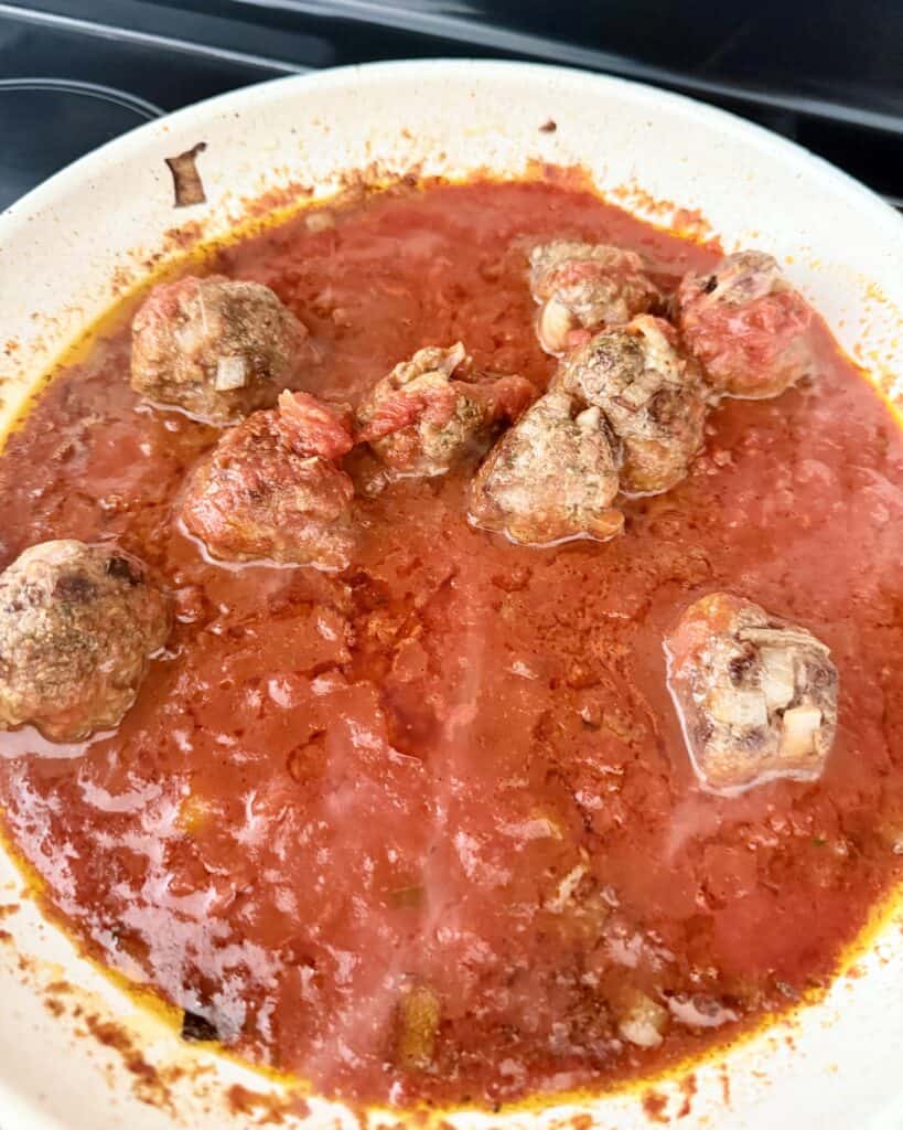 fully cooked meatballs in tomato suace in a pan on the stove top.