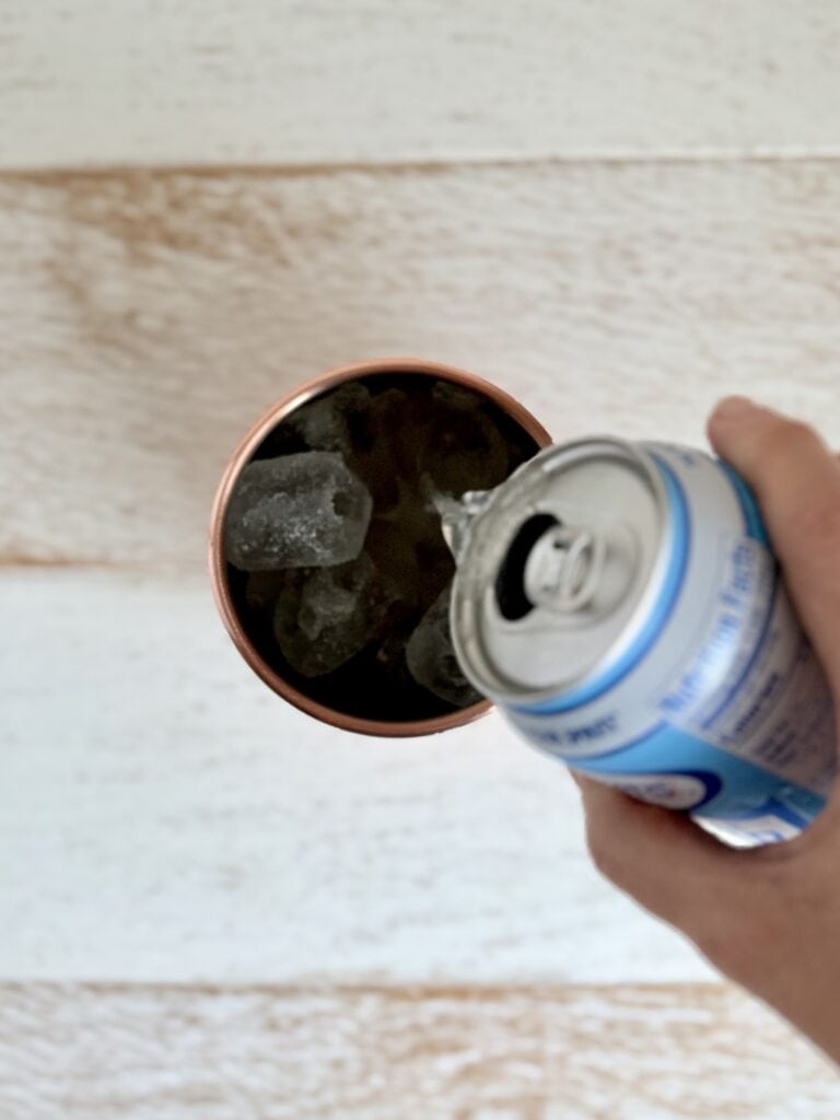 Ginger beer being poured into a copper Moscow Mule mug filled with ice.