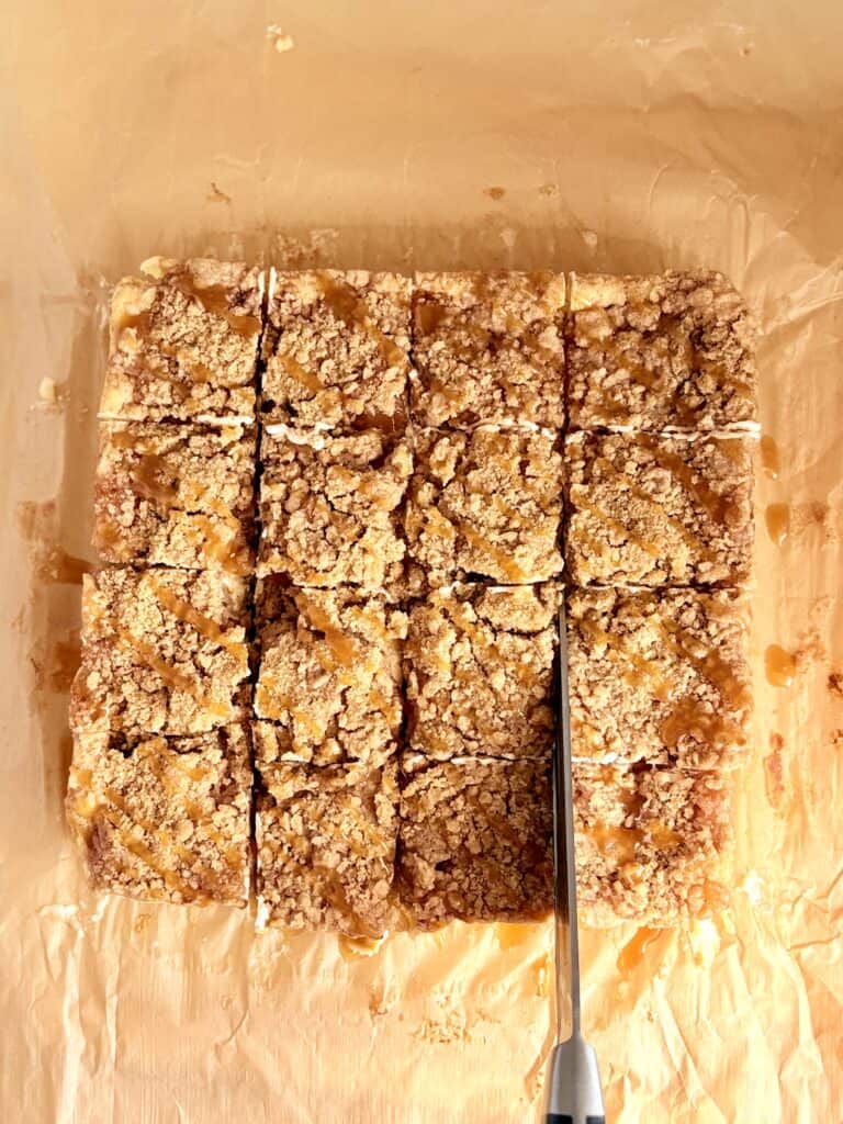 Caramel Apple Cheesecake Bars being cut into squares with a knife