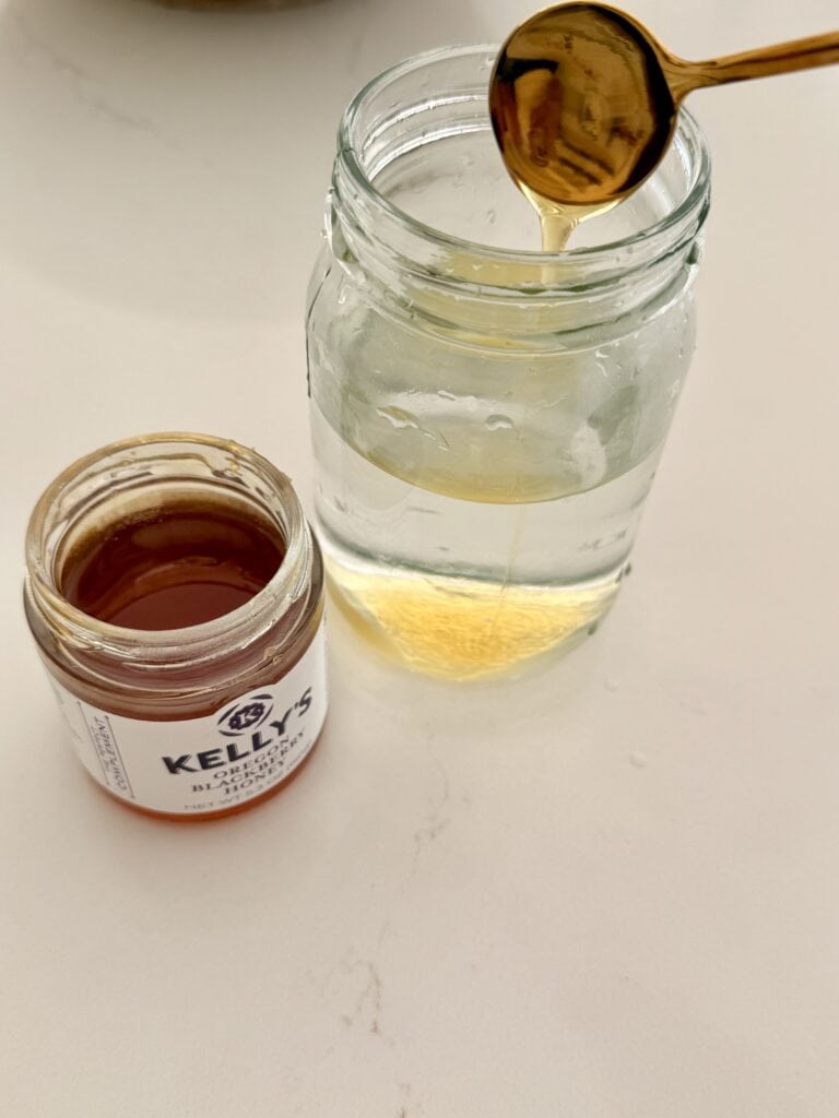 Honey being added to a jar of warm water for no-knead bread dough.