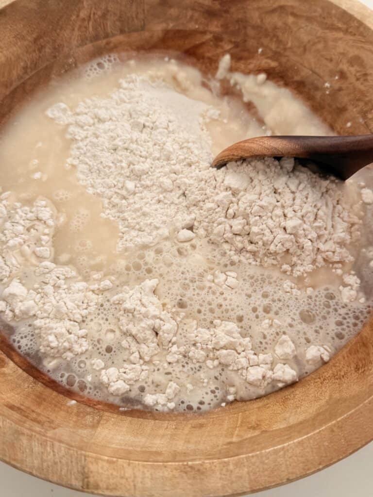 Stirring the wet no-knead bread dough with a wooden spoon.
