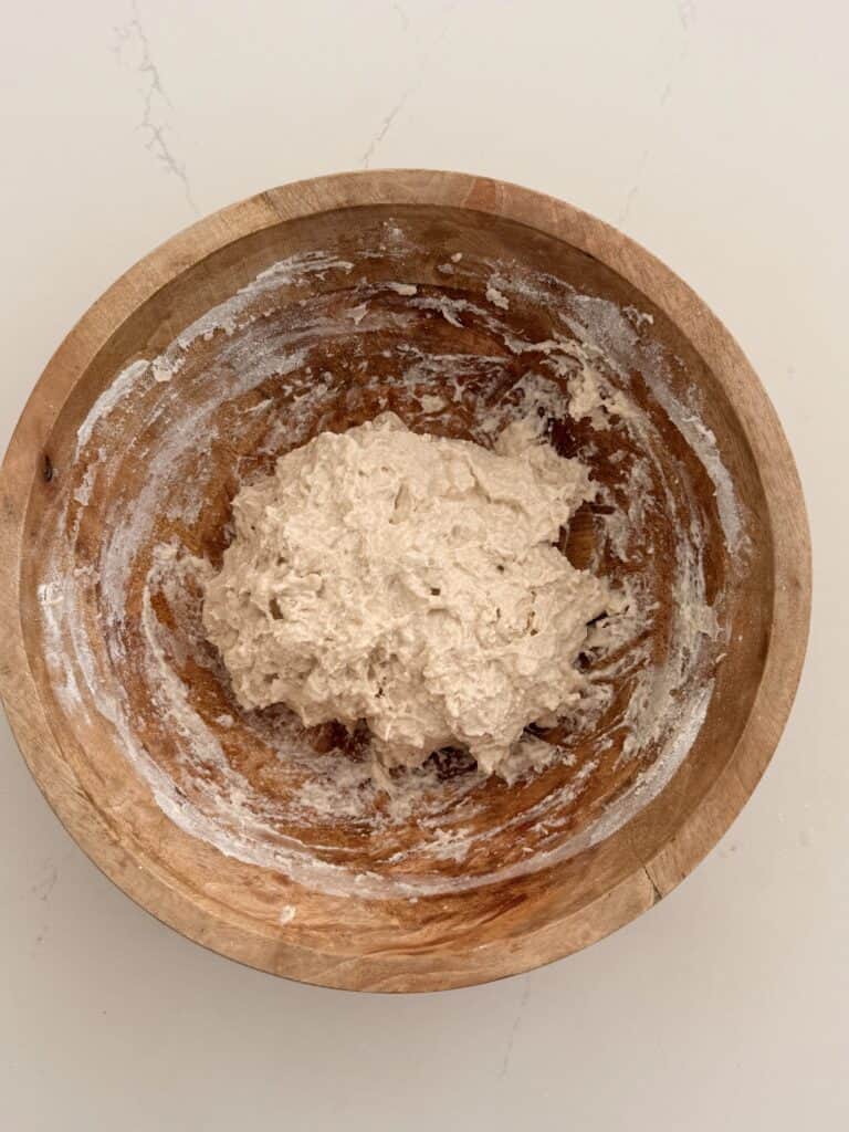 Wet, shaggy no-knead bread dough in a wooden mixing bowl.