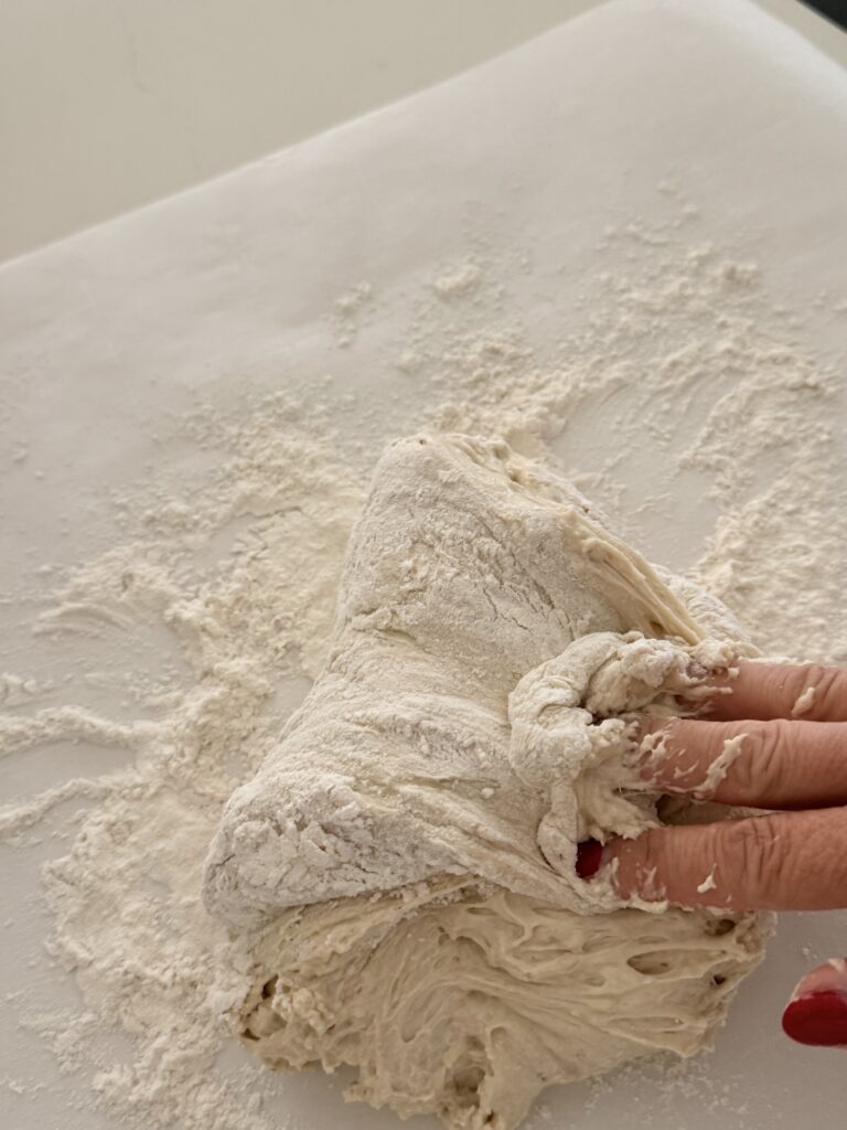 Shaping sticky no-knead bread dough on a floured work surface.