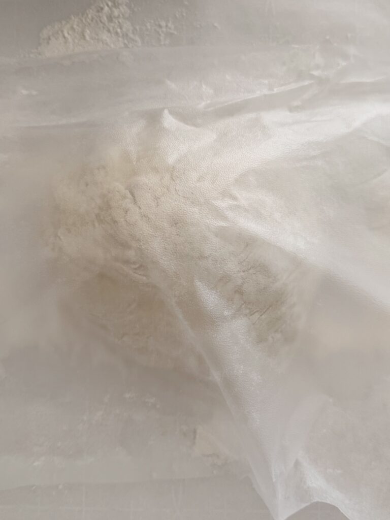 Unbaked bread dough wrapped in parchment paper covered by plastic wrap.