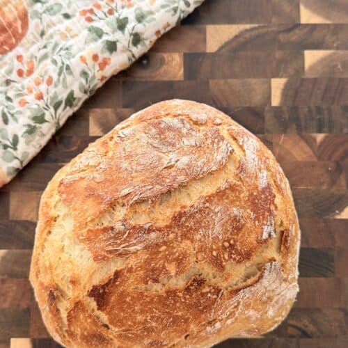 Freshly baked homemade Dutch oven bread with a crusty golden exterior on a wooden cutting board.