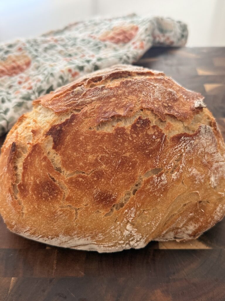 Round loaf of no-knead Dutch oven bread with a crisp, deeply golden crust.