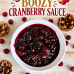 Close-up of homemade boozy cranberry sauce in a white bowl with fresh cranberries and pinecones on a wooden table.