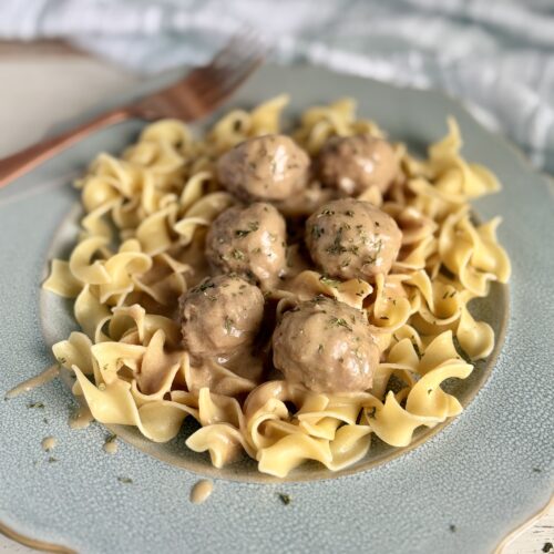 Swedish meatballs and cream sauce over egg noodles on a blue plate next to a kitchen towel.