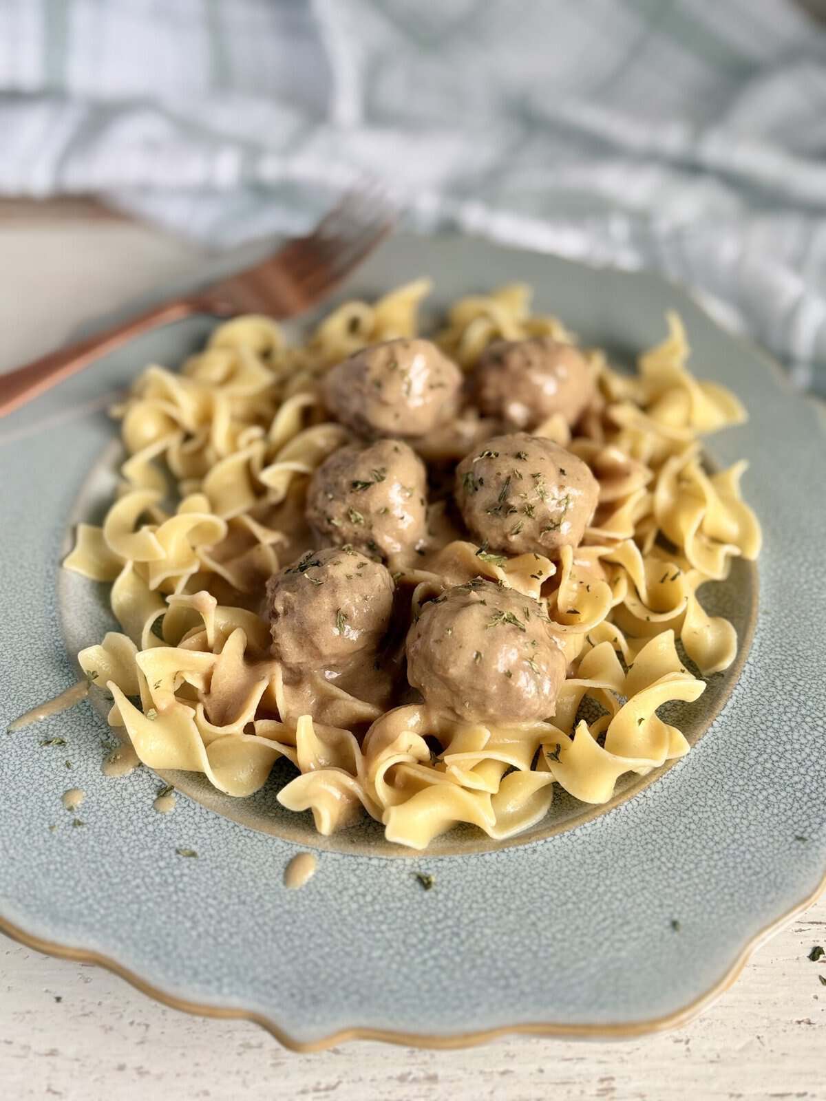 Swedish meatballs and cream sauce over egg noodles on a blue plate next to a kitchen towel.