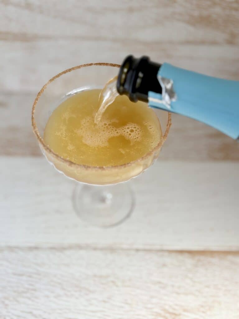 Prosecco being poured into a couple glass with apple cider and a cinnamon sugar rim.