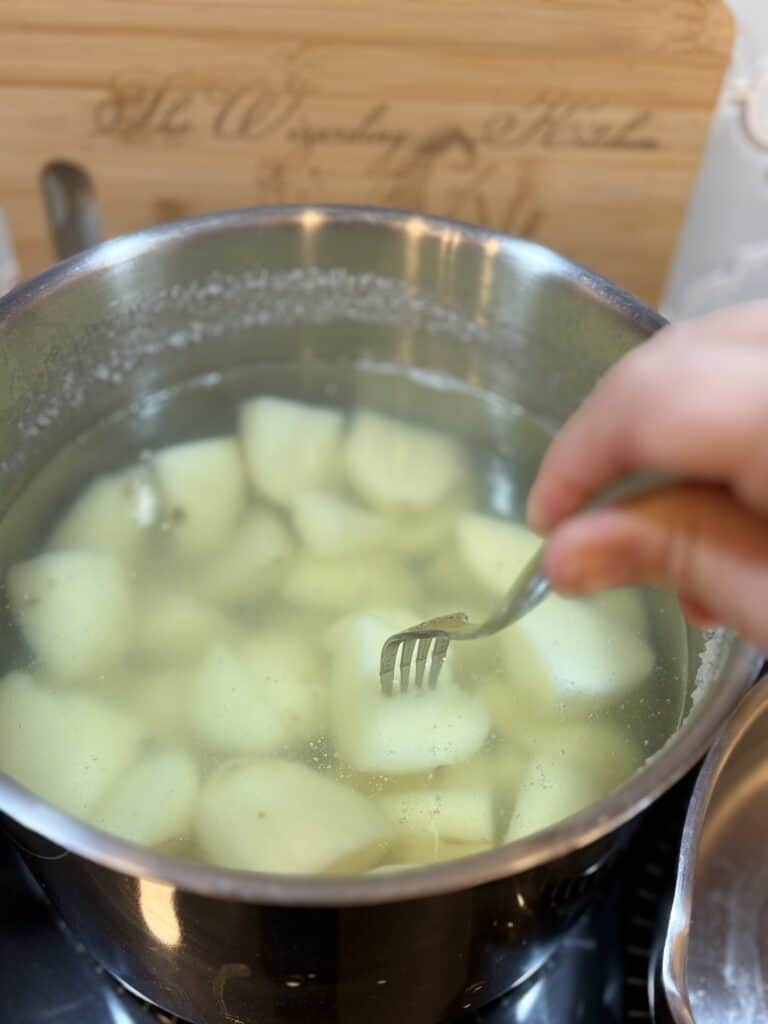 Potatoes in boiling water in a large pot being pierced with a fork.