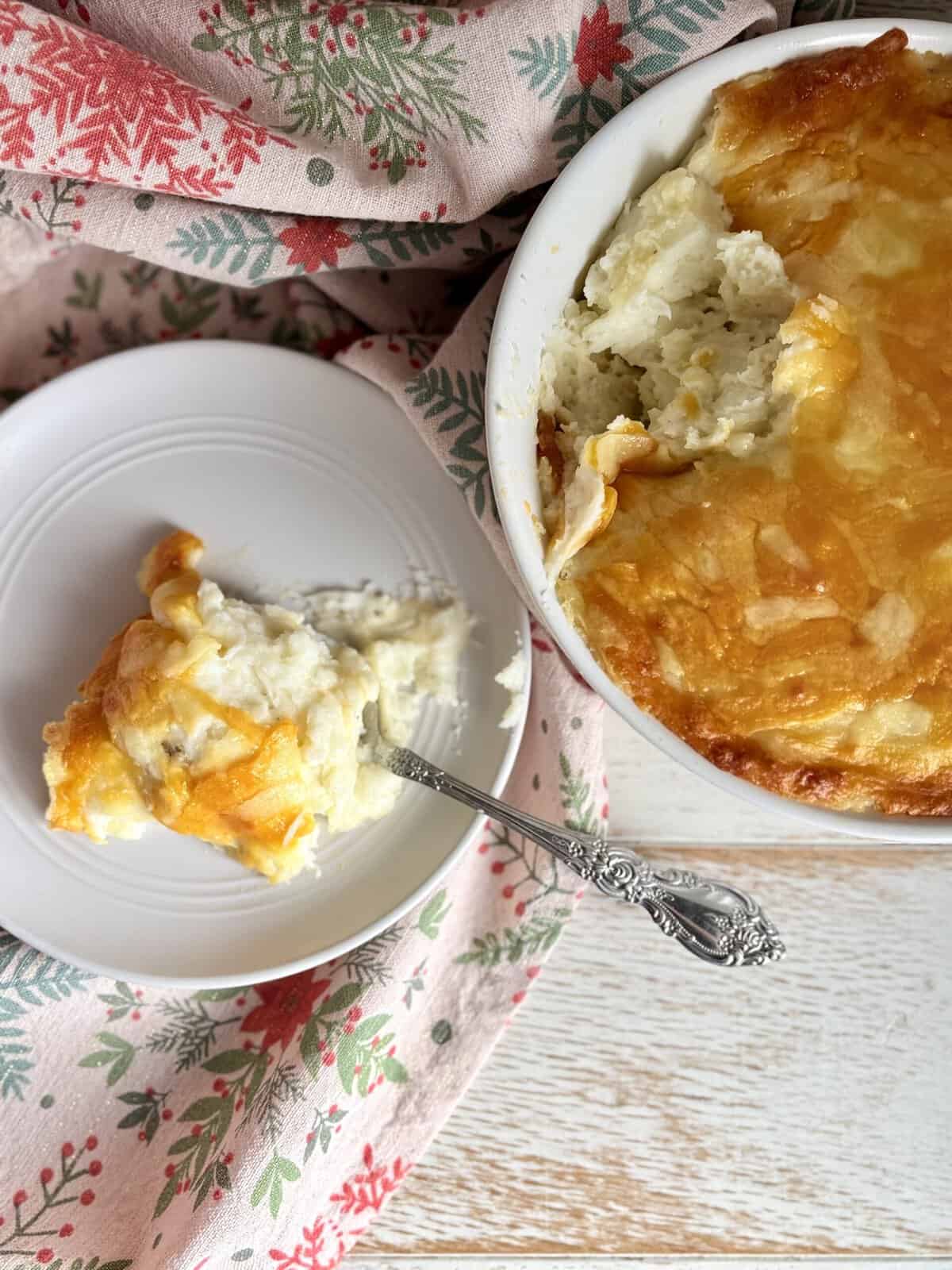 Cheesy mashed potatoes in a bowl next to a white plate with a silver spoon.