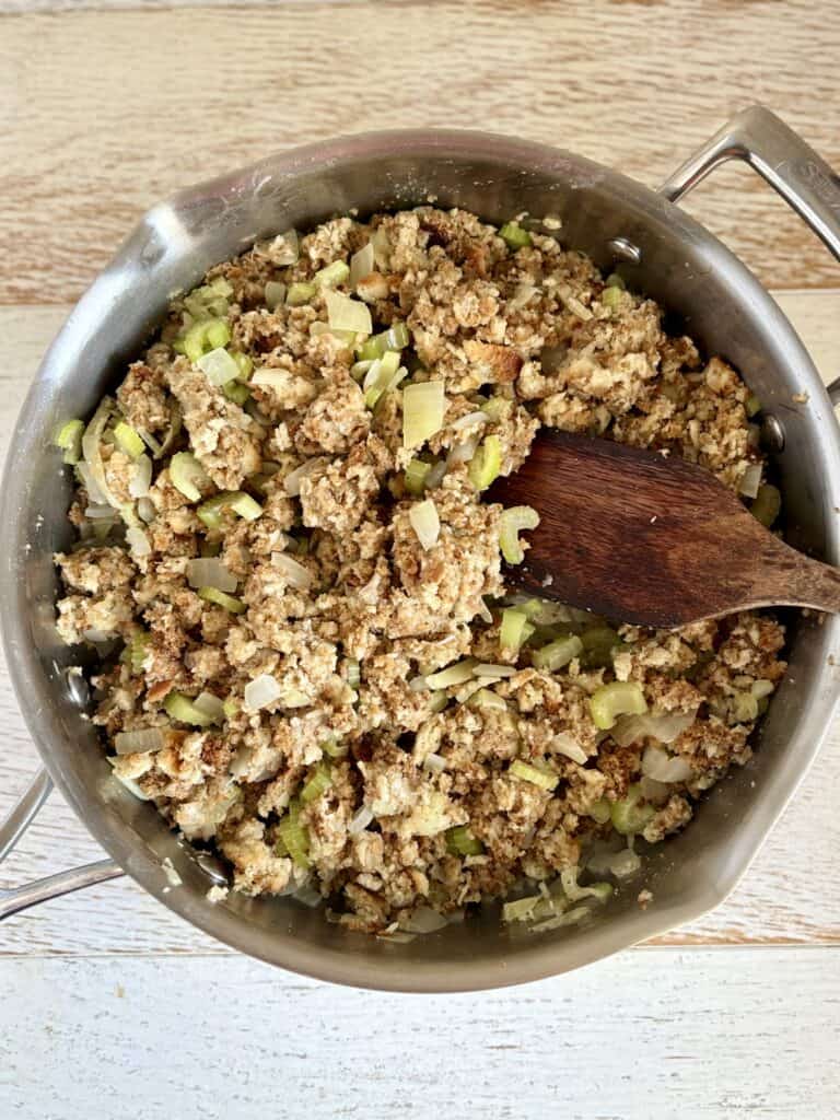 Stuffing cooked chopped celery in a stainless steel skillet, ready for further preparation, on a wooden surface.