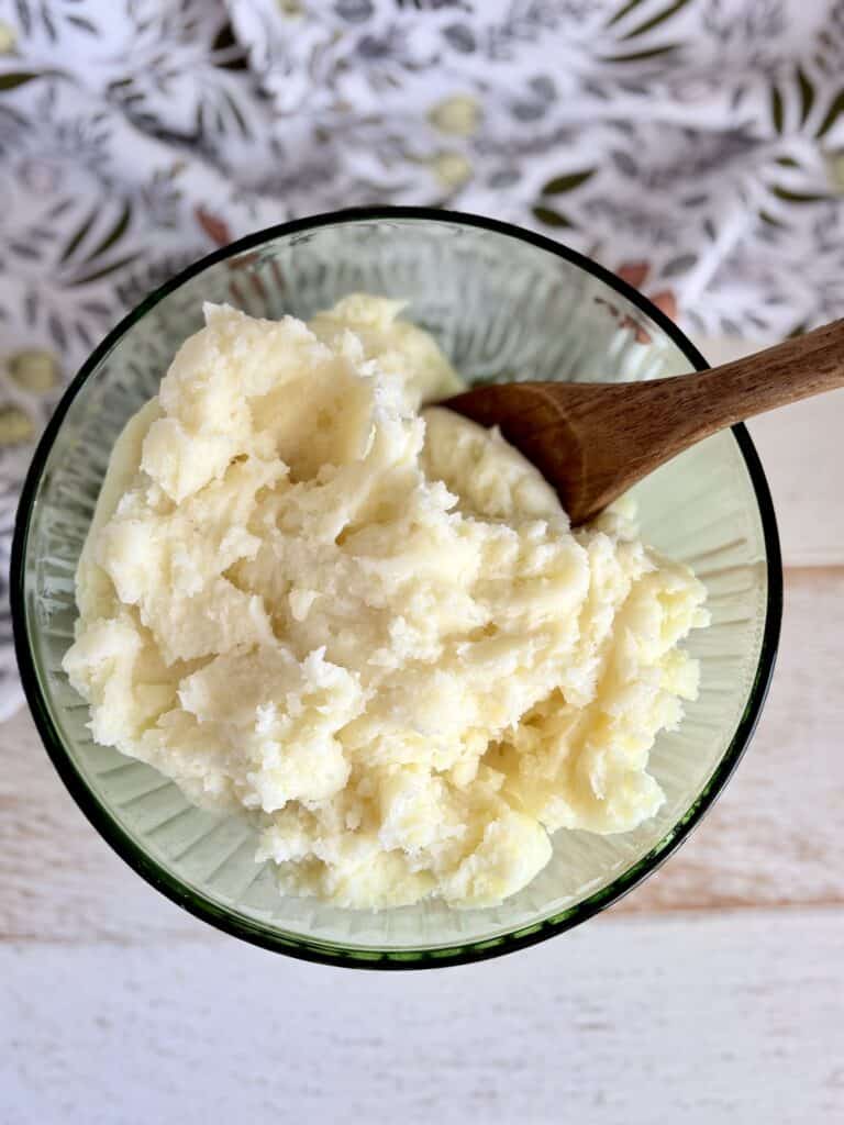 A bowl of creamy mashed potatoes with a wooden spoon, perfect for comfort food and side dishes.