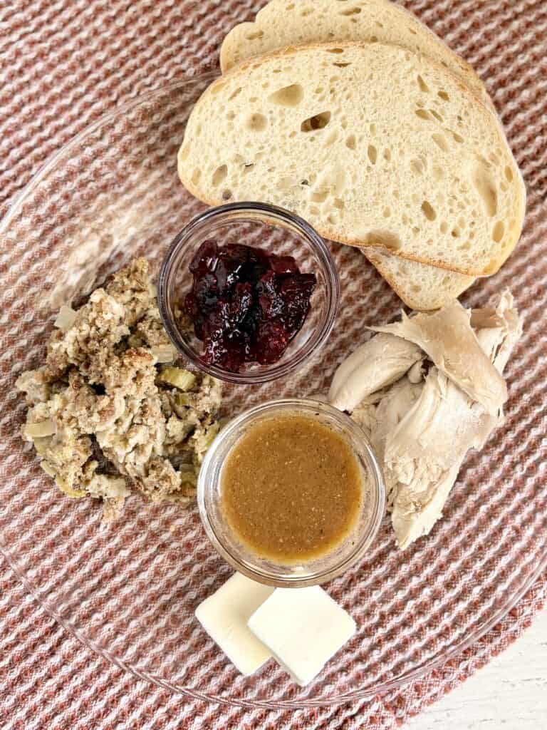 Fresh bread slices served with jam, chicken, honey mustard, and butter on a glass plate for a simple homemade meal.