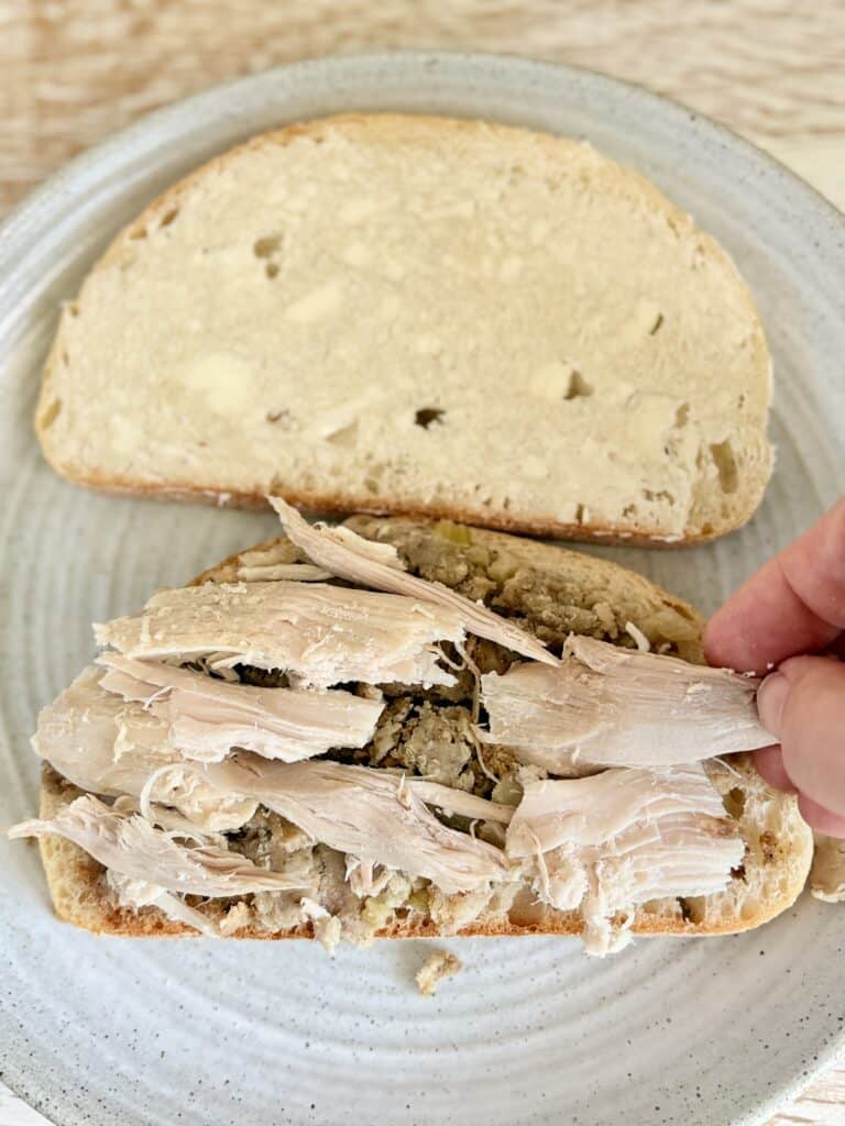 Close-up of a homemade turkey sandwich with shredded turkey and whole grain bread on a light blue plate.