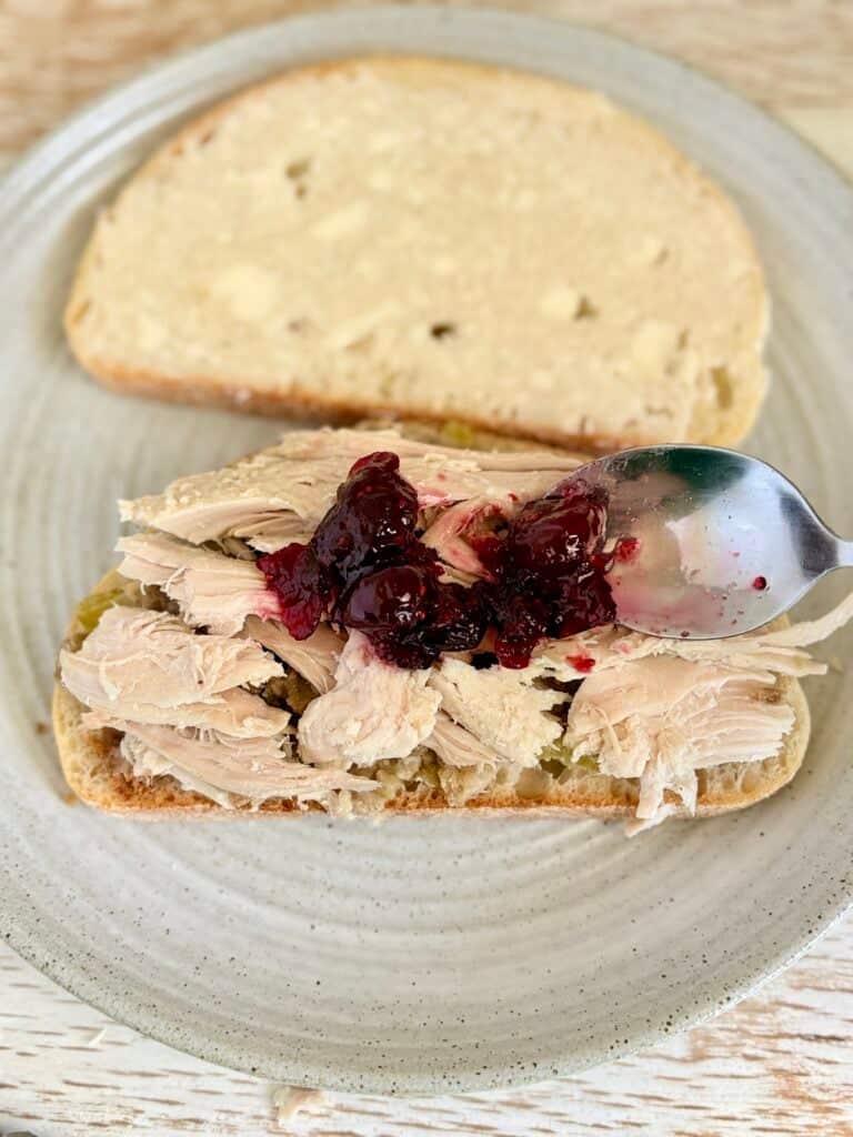 Close-up of a turkey sandwich with cranberry sauce on a plate, with a slice of bread in the background, perfect for lunch or dinner.