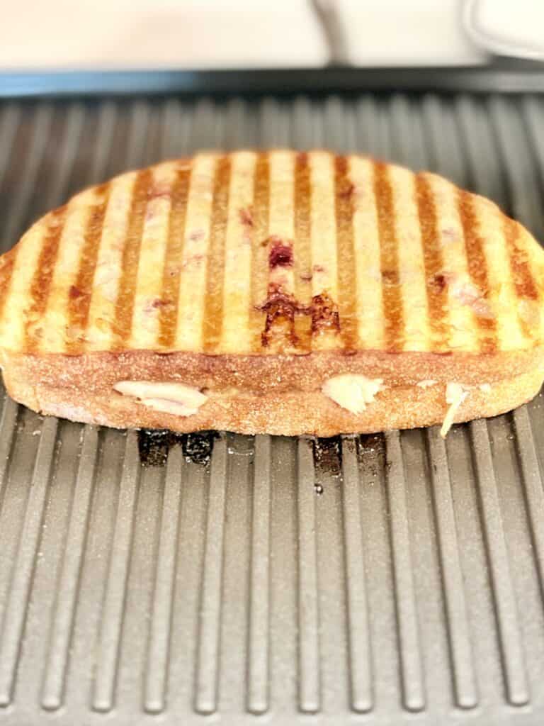 Close-up of a grilled sandwich with melted cheese and grill marks on a ridged panini press.