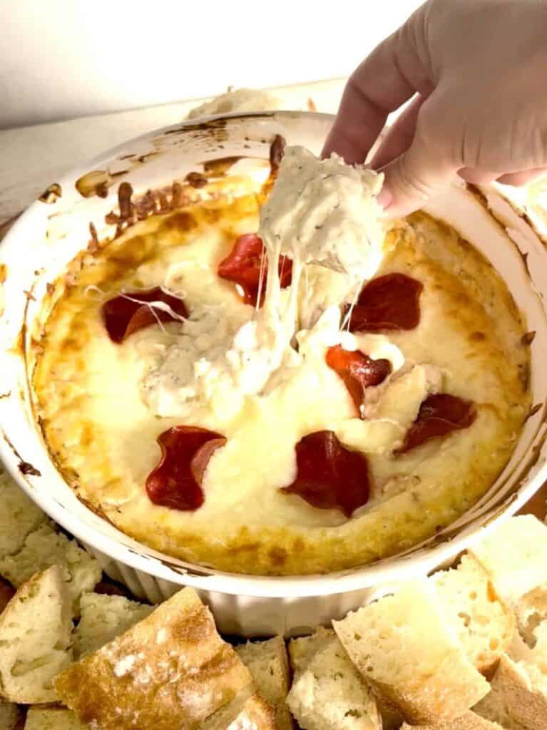 a hand dipping bread into creamy white pizza dip