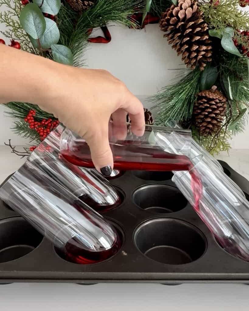 Person pouring cranberry pomegranate mixture into a silicone mold for holiday drinks, with festive wreath in background.
