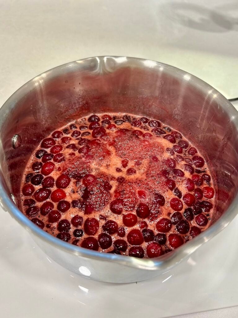 Close-up of a pot filled with freshly made cranberry sauce with whole cranberries and a vibrant red color.
